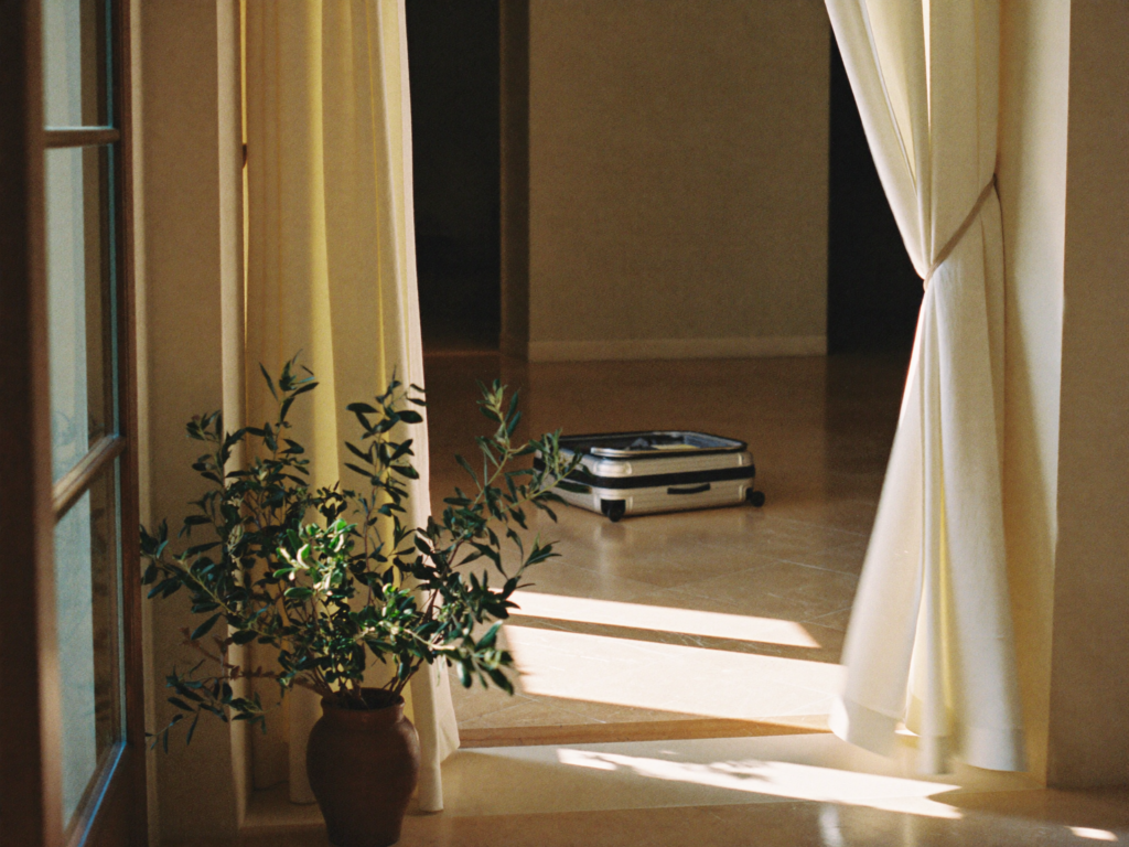 A sunlit stone entrance hall at a private villa, a single suitcase set down.