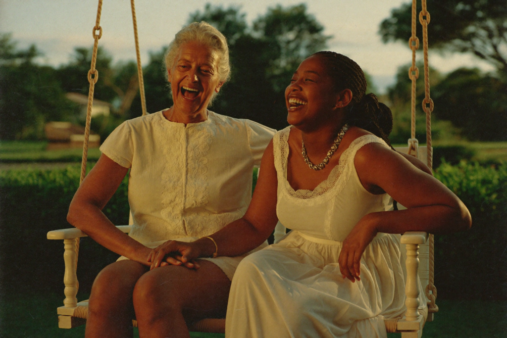 A mother and her adult daughter laughing together on a porch swing at golden hour.